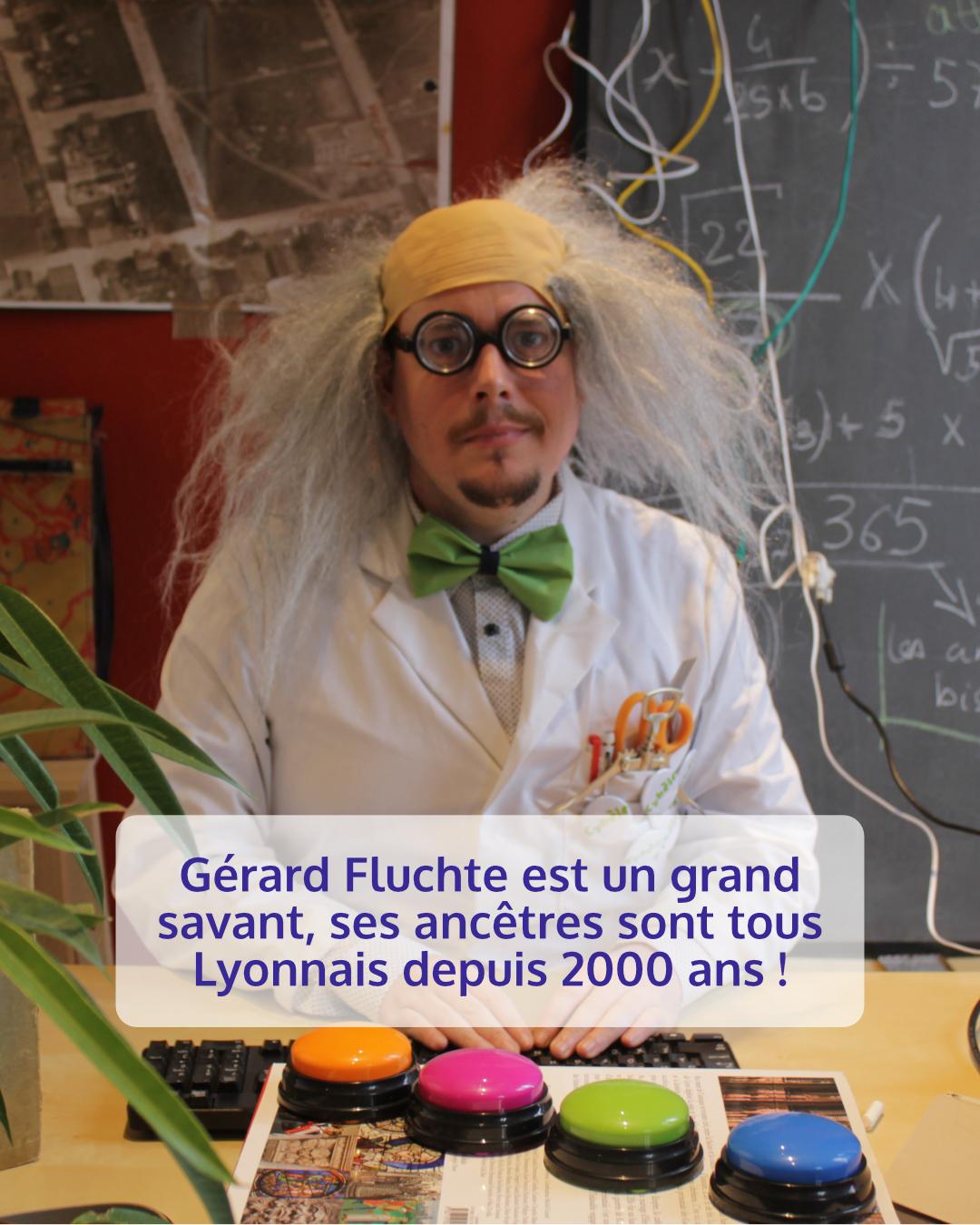 Photo d'un homme déguisé en savon, avec une perruque des grosses lunettes, une blouse et un nœud papillon vert derrière lui, un tableau avec des formules mathématiques devant lui sur la table, des buzzers colorés.
Légende : Gérard Fluchte est un grand savant. Ses ancêtres sont tous lyonnais depuis 2000 ans !